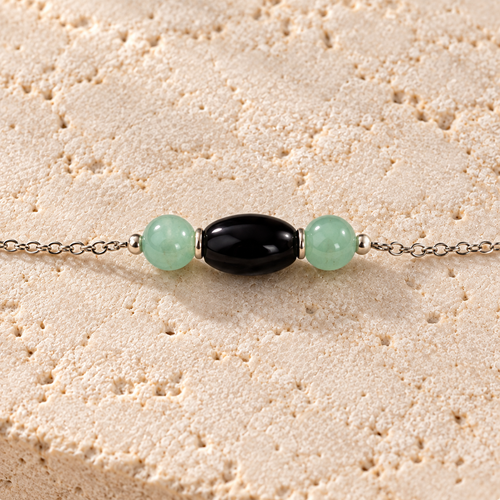 Close-up of the black oval bead and two mint beads on a fine silver chain, resting on ivory stone.
