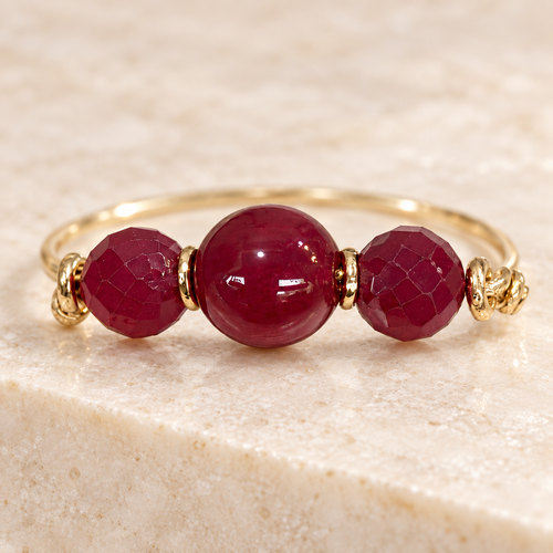 Three deep red beads with gold-tone wirework on warm ivory stone.